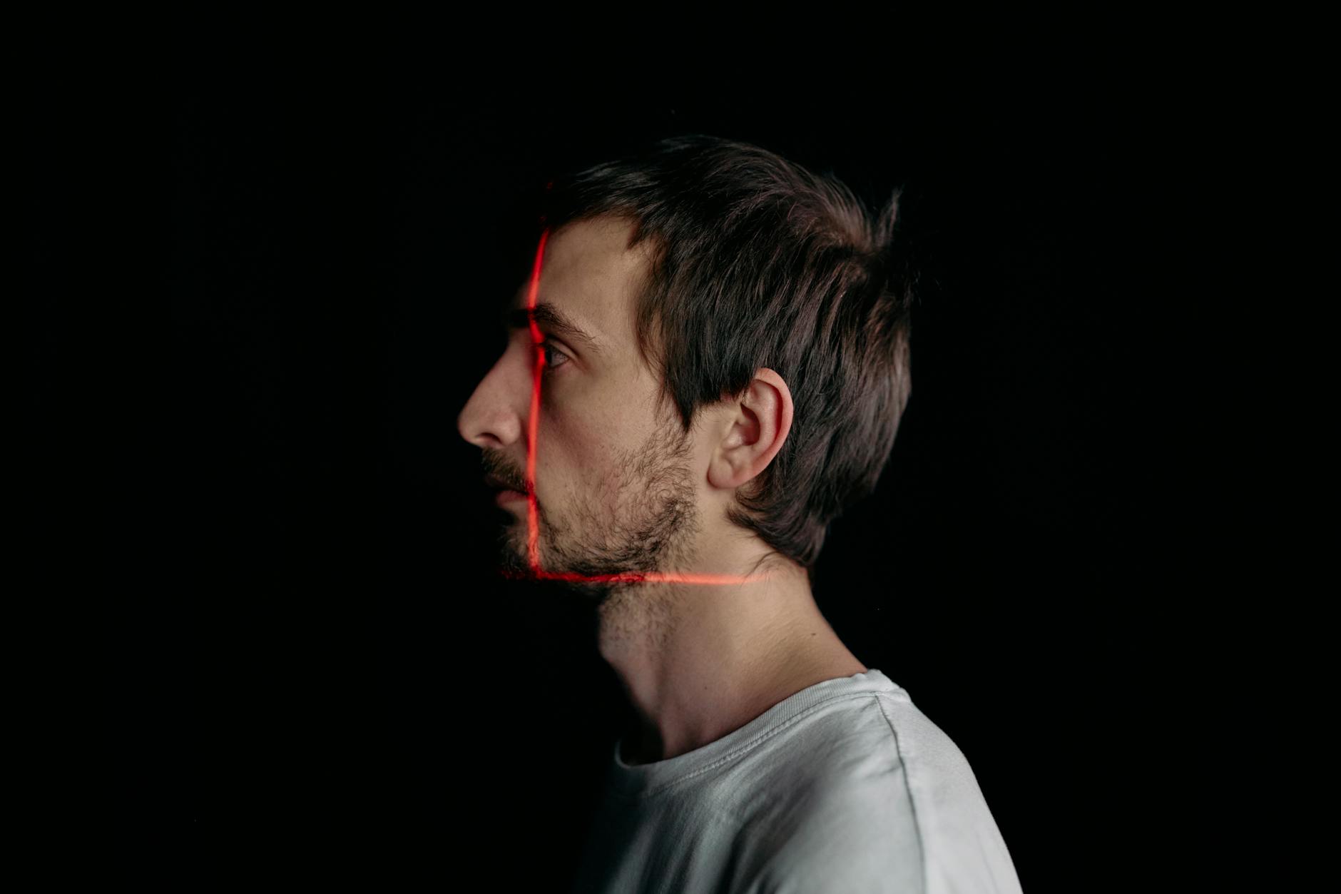 Side profile of a man with red laser scanning lines on his face on a black background.