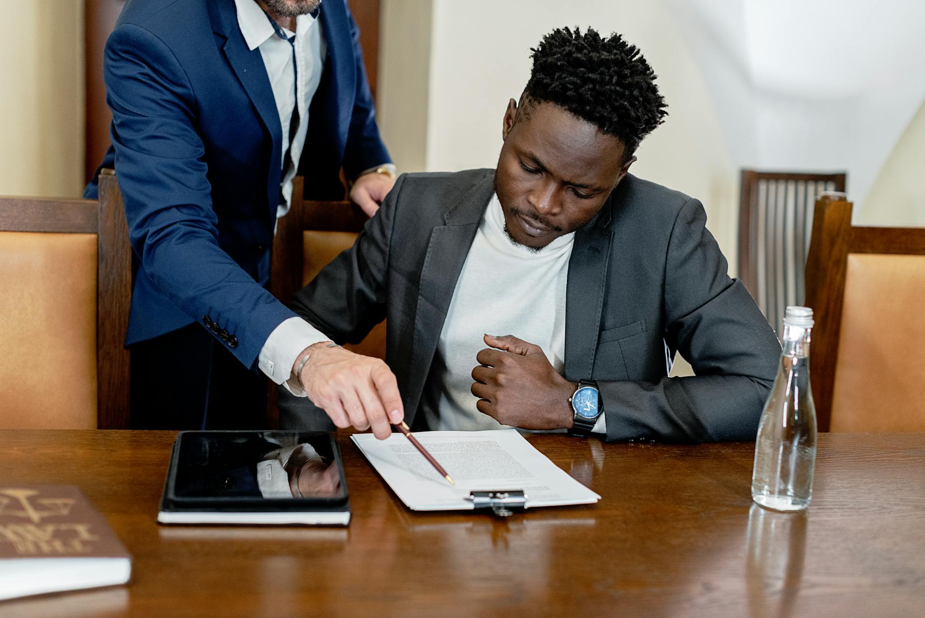 Two businessmen in a legal consultation reviewing a document with a tablet on the desk.